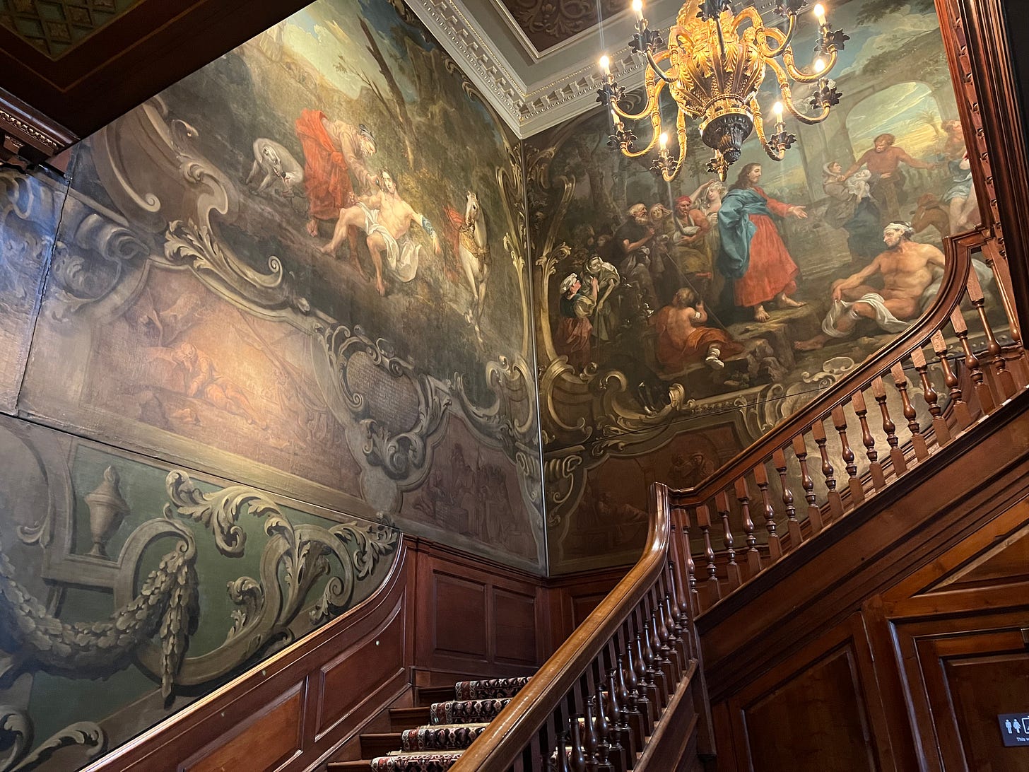 An elegant staircase with a wooden banister. Massive history paintings are on the walls behind it. An elegant staircase with a wooden banister. Massive history paintings are on the walls behind it.