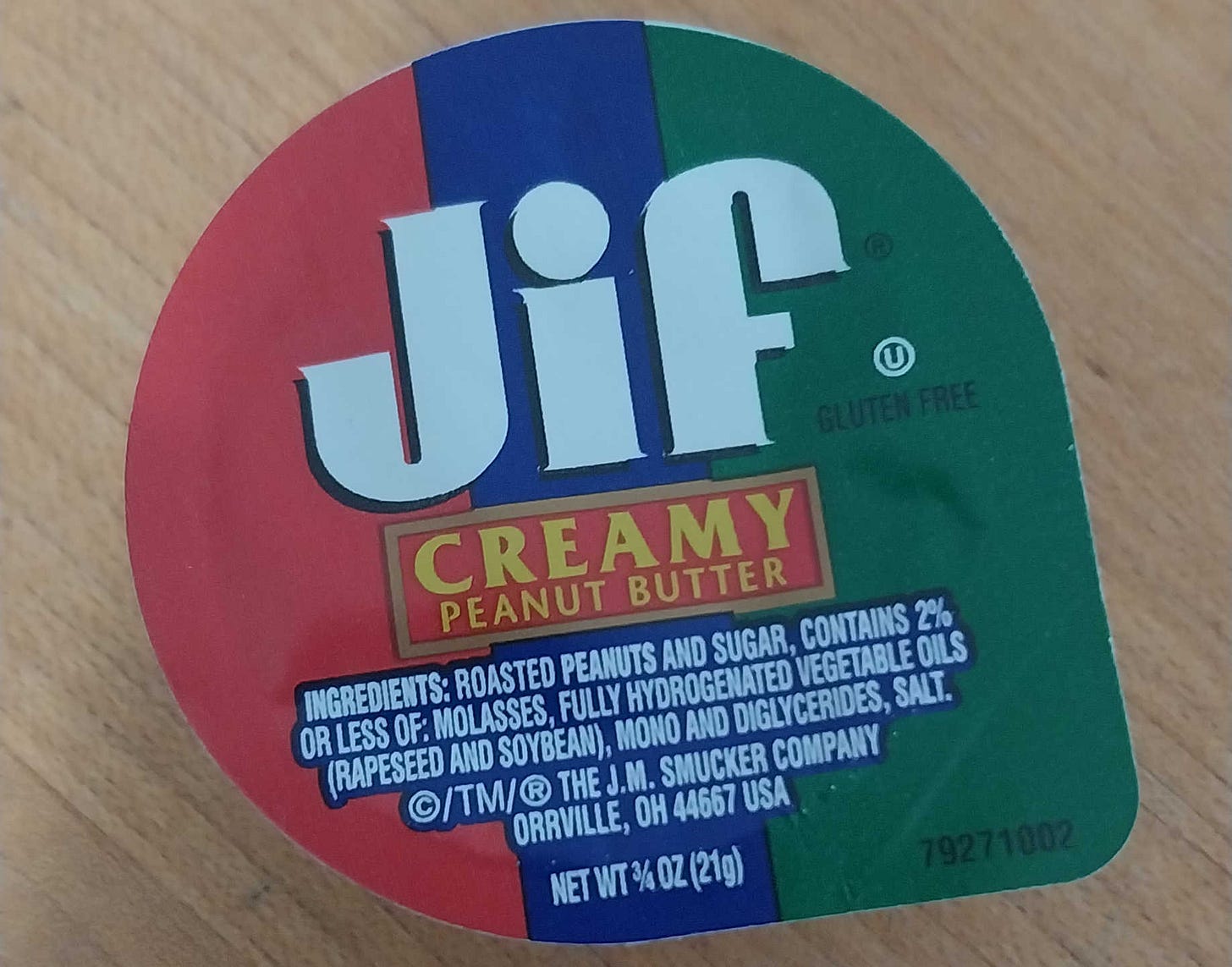 A three-quarter ounce container of Jif "CREAMY PEANUT BUTTER," with "INGREDIANTES: ROASTED PEANUTES AND SUGAR, CONTAINS 2% OR LESS OF: MOLASSES, FULLY HYDROGENATED VEGETABLE OILS (RAPESEED AND SOYBEAN), MONO AND DIGLYCERIDES, SALT."