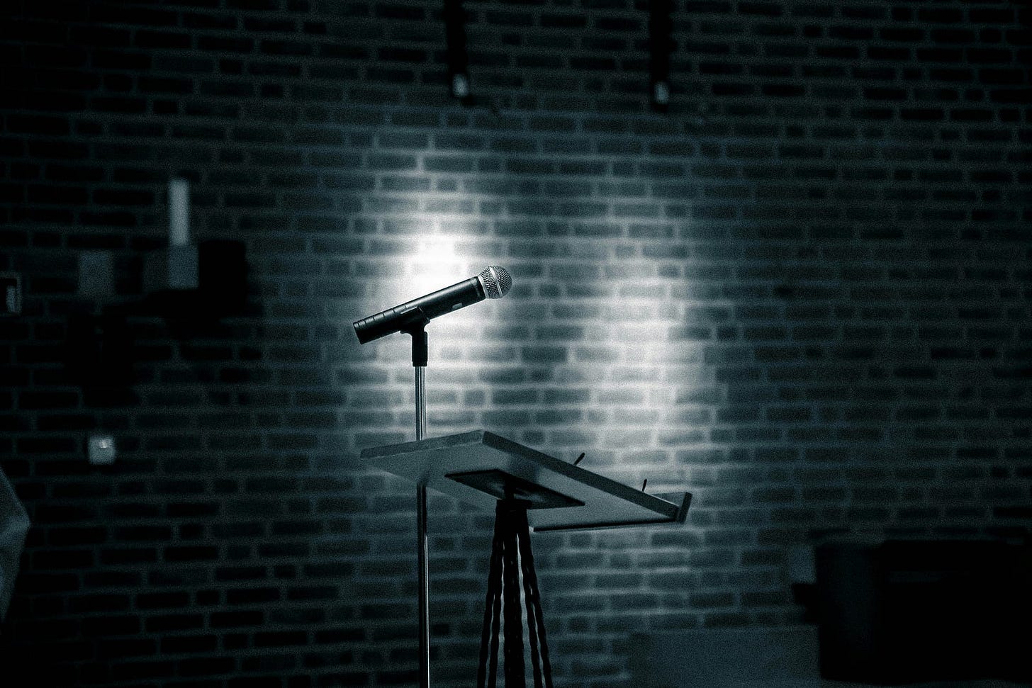A dimly lit stage, photographed in black and white. A mic and a podium are backlit by two spotlights, awaiting the talent.