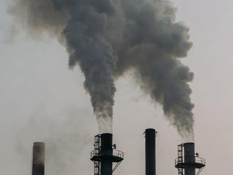 A photograph of industrial smokestacks emitting smoke into a hazy, overcast sky, emphasizing pollution. A photograph of industrial smokestacks emitting smoke into a hazy, overcast sky, emphasizing pollution.