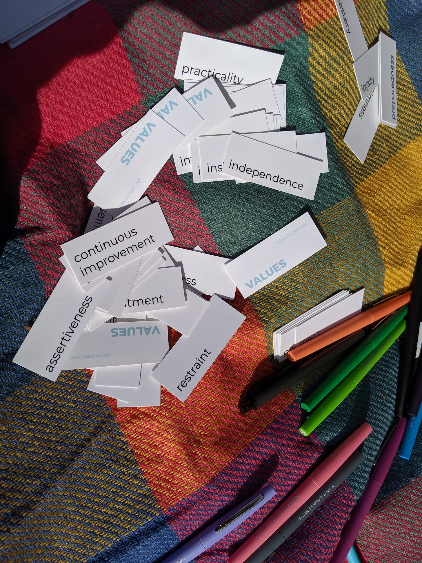 Image shows a set of small cards spread on a picnic rug in the sunshine. Some of the cards have the word ‘values’ written on them. Others have different single words on them, such as practicality, independence, continuous improvement, assertiveness, and restraint. There are coloured pens scattered around them.