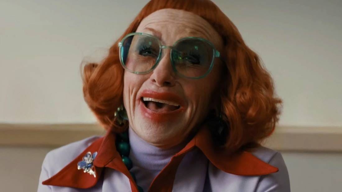 Amy Madigan as Aunt Gladys in Weapons. She grins dementedly, wearing a red wig with a very high and severe fringe