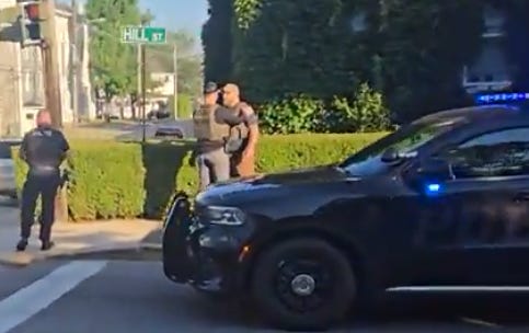 A video clip of the scene shortly after the shooting shows one ICE officer appearing to console another. The victim is lying on the pavement just out of the left frame of this image. (Frame grab of video posted by @gremloe to x.com)