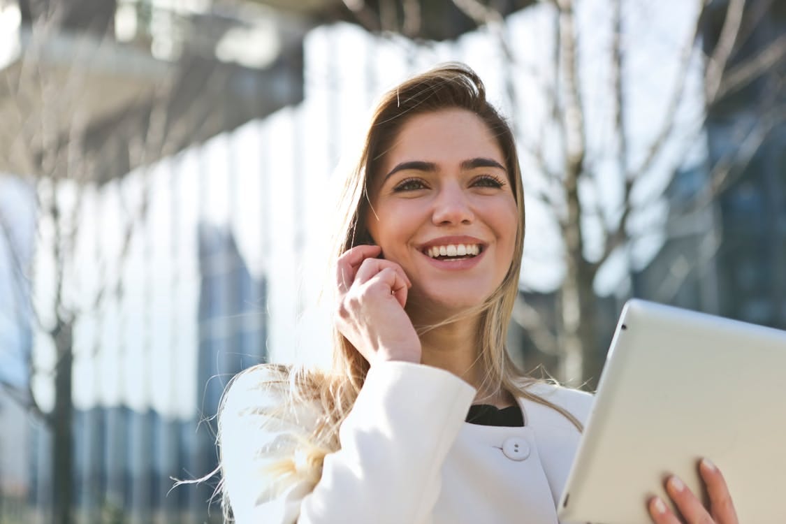 Free Confident businesswoman using her tablet and phone, smiling outdoors in sunlight. Stock Photo