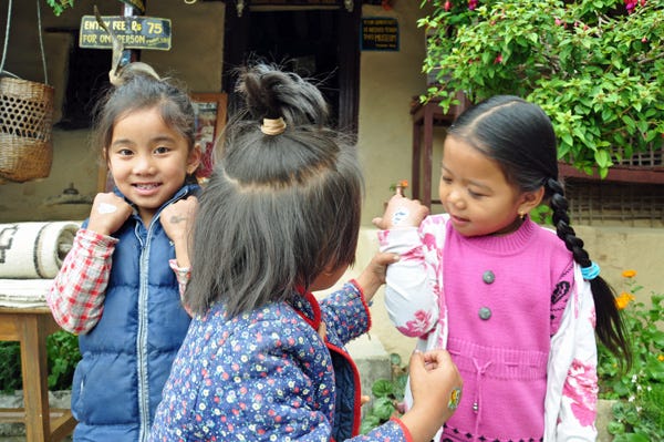 Three little girls wearing jackets with stickers on their hands. Two are looking at the camera and one has her back turned. 
