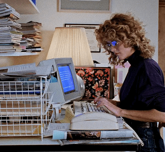 This may contain: a woman is typing on her computer in an office with stacks of books and magazines