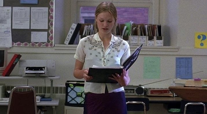 This may contain: a woman standing in front of a desk holding a book