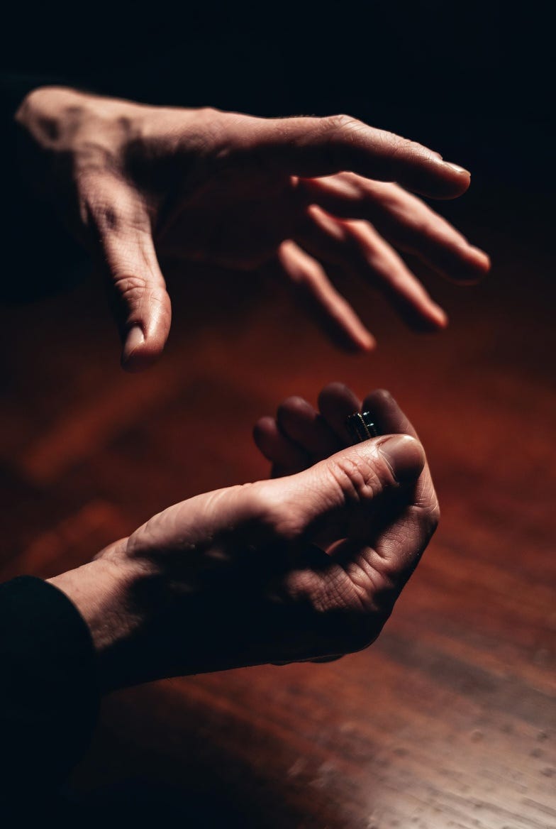 A photograph of a magic trick performance featuring the "Denying Death" sleight, with hands and object in a dimly lit, dramatic setting.