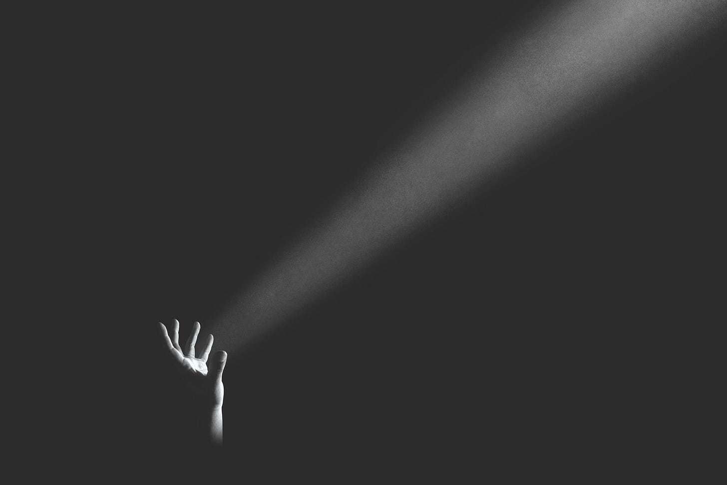 a hand reaching for a ray of light in a dark room