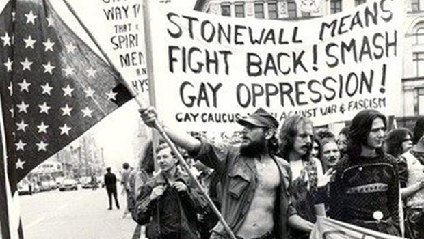 A black and white photograph of queer folks with signs and posters, walking the streets of NYC.
