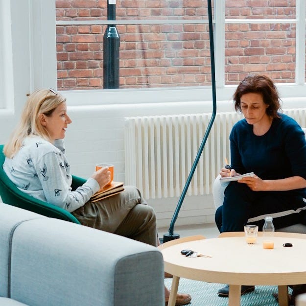 two woman sits on sofa chairs inside house