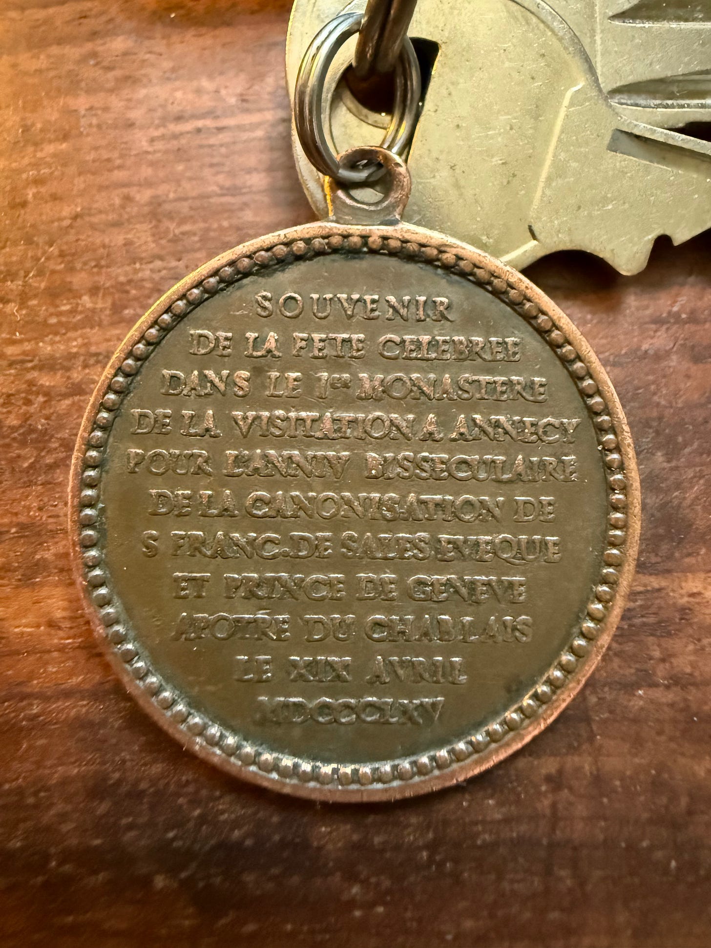 A medal on a key chain. On the front, an image of a bald dude with a long beard and pectoral cross, with the inscription of "St. Francisce a Salesio, Ora Pro Nobis". On the back: "Souvenir de la fete celebrate dans le 1st monastere de la visitation a Annecy pour l'anniv bisseculaire de la canonisation de S Franc. De Sales, eveque et France de Geneve apogee du Chablis le XIX Avril MDCCCLXV