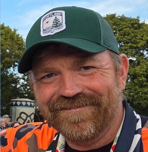 Platner outdoors with beard and a Portland hat; he is smiling Platner outdoors with beard and a Portland hat; he is smiling