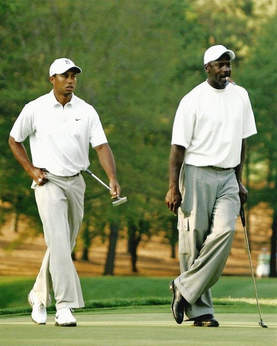 This may contain: two men in white shirts and gray pants walking on a golf course with trees behind them