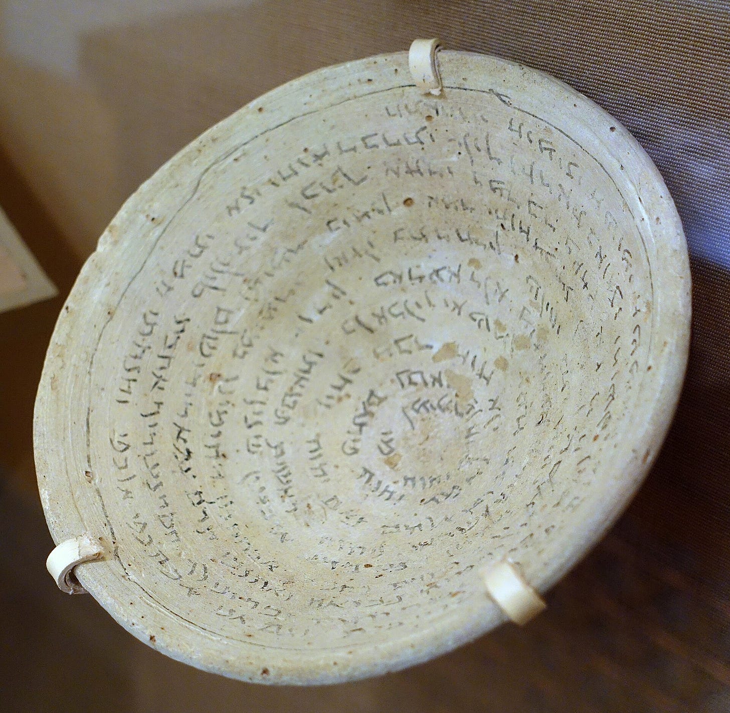 A shallow clay bowl seen from above, its inside covered with a spiral of handwritten Aramaic lines. A shallow clay bowl seen from above, its inside covered with a spiral of handwritten Aramaic lines.