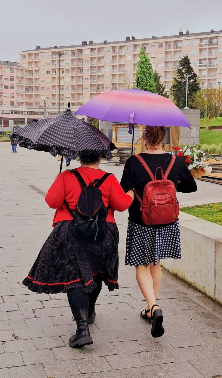 Two femme people in dresses walking under umbrellas in the city on a rainy day Two femme people in dresses walking under umbrellas in the city on a rainy day