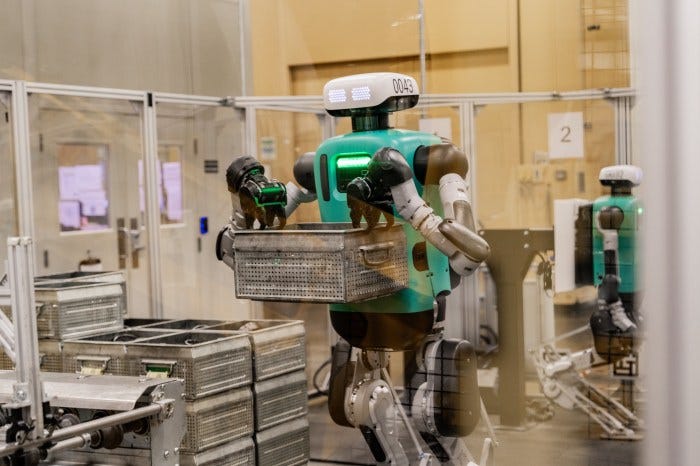 Humanoid robot "Digit" carrying a container in a manufacturing plant.