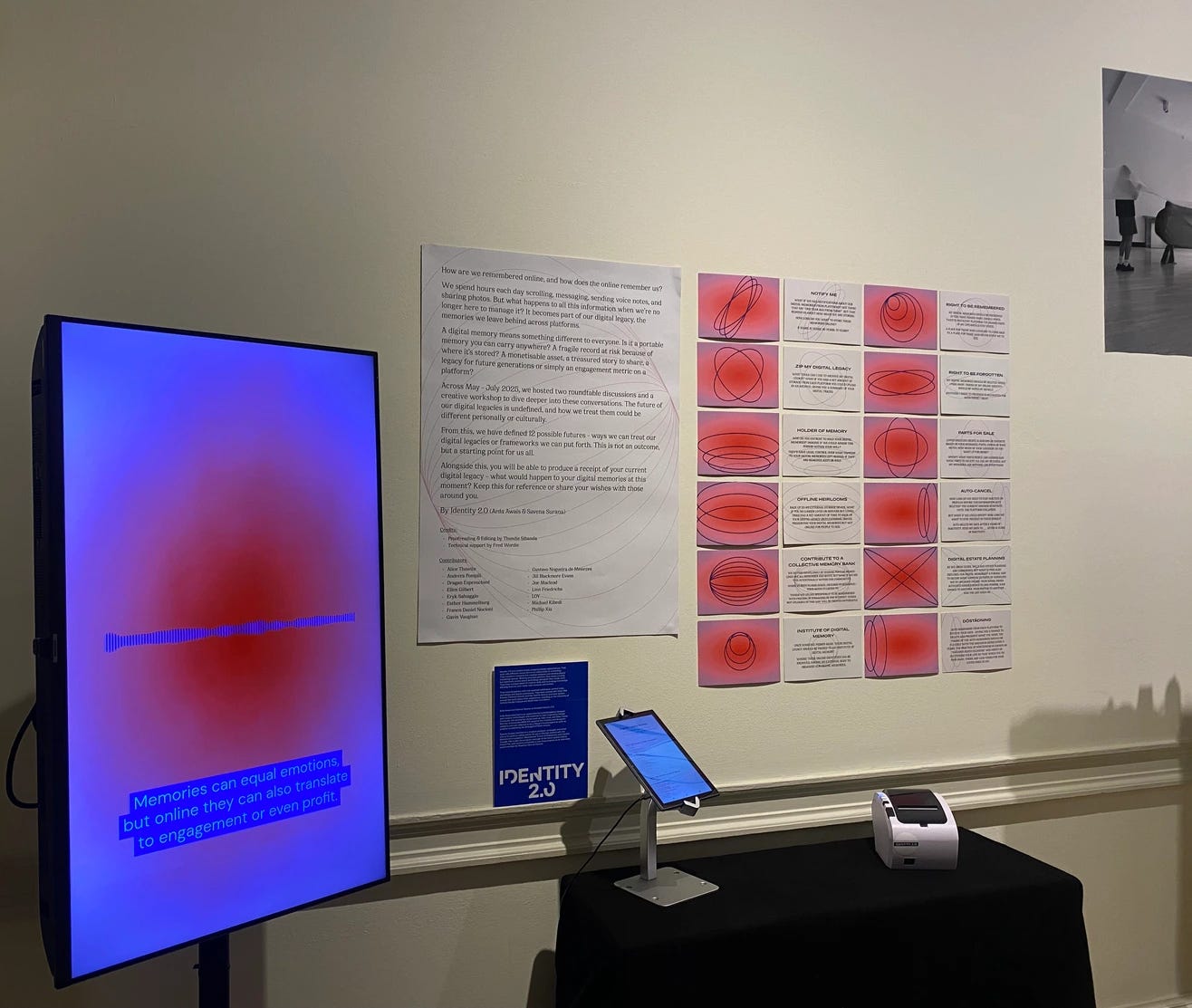 An exhibition in a gallery space with white walls showing a large computer screen and red and white posters in a series of 12 on the wall. An exhibition in a gallery space with white walls showing a large computer screen and red and white posters in a series of 12 on the wall.