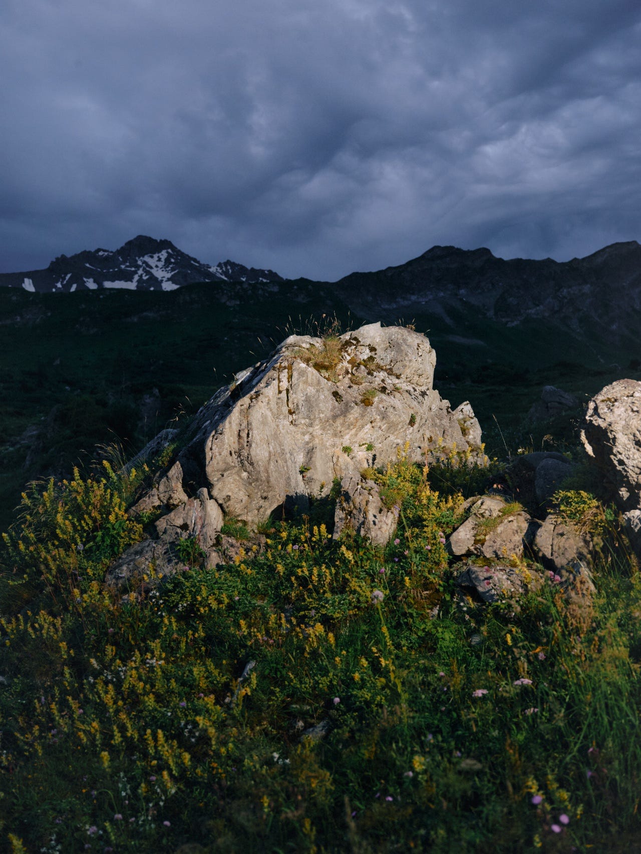 A pale boulder lit against dark mountains and a heavy, overcast evening sky.