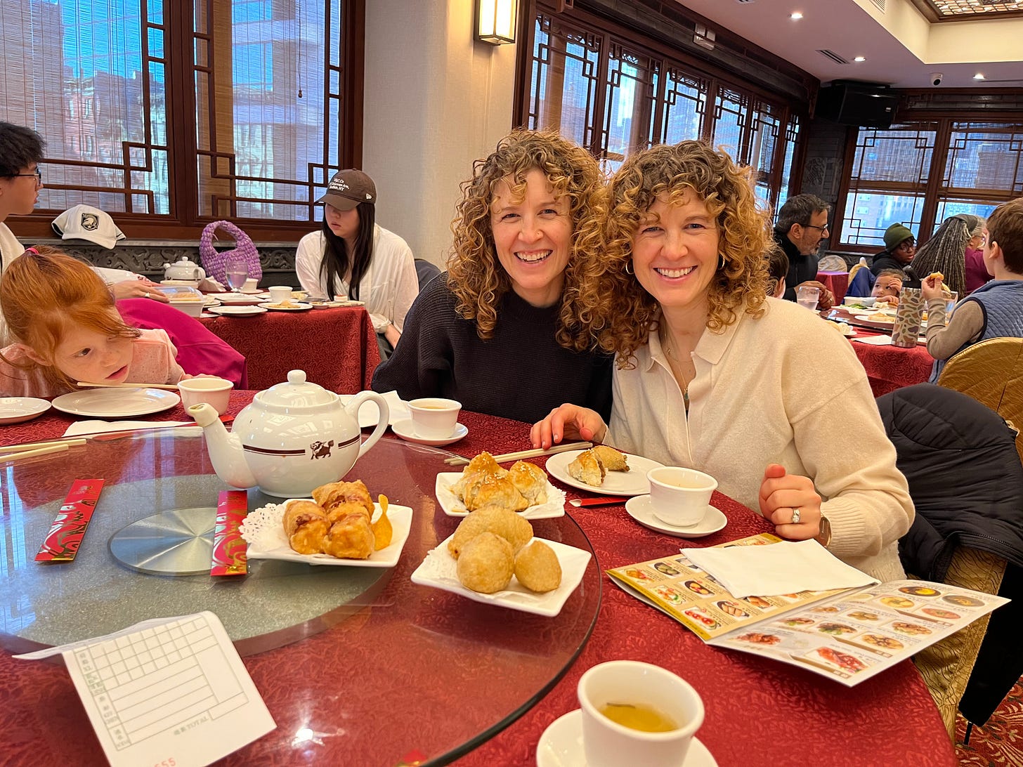 Two women sitting at a table in a Chinese restaurant, with plates of Chinese food set out in front of them.