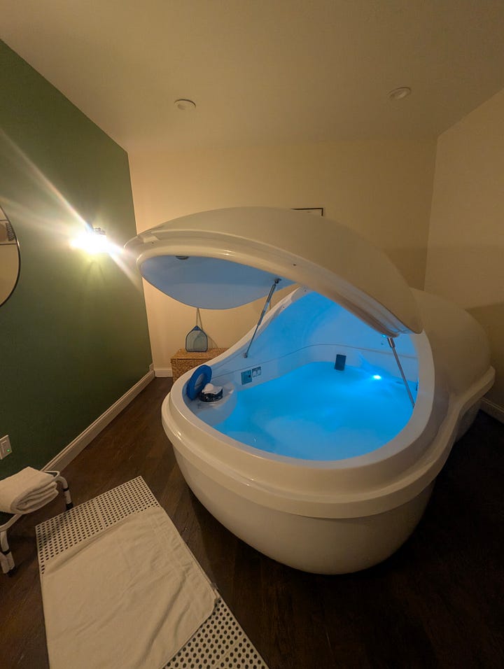 Pills on a granite countertop, arranged like a raised middle finger. A float pod in a room with a white bathmat. The pod lid is open, exposing blue water.