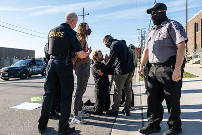Photographic evidence of my arrest. I'm standing as police cuff me. A pastor kneels in prayer to my left as an ICE agent attempts to get him to move out of the way.