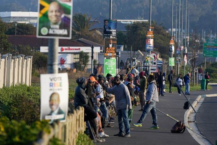 Job seekers sit beneath campaign posters for the South African general elections, in Cape Town