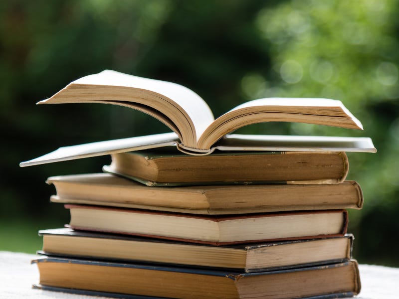 A stack of books sits on an outdoor table on a sunny day.