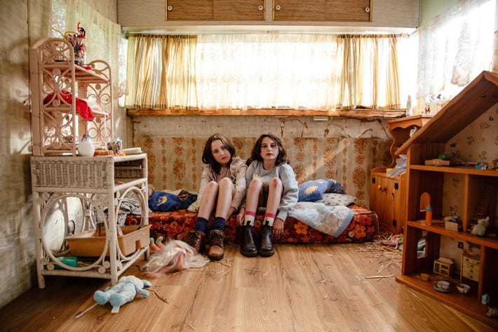 two young girls sit side by side inside a caravan filled with toys