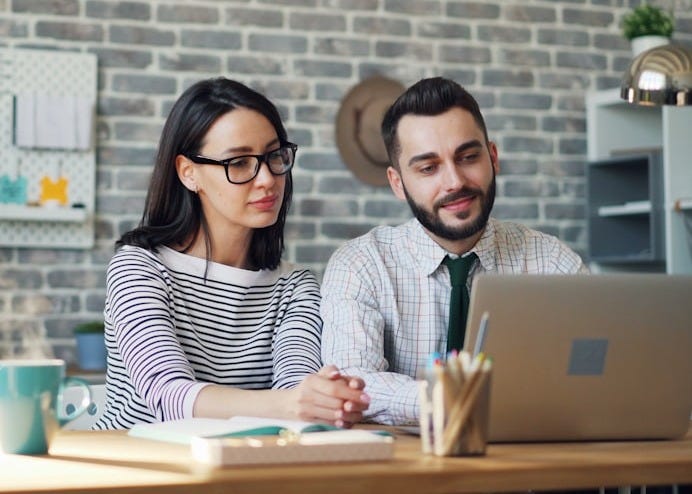 a man and woman sitting at a table looking at a laptop