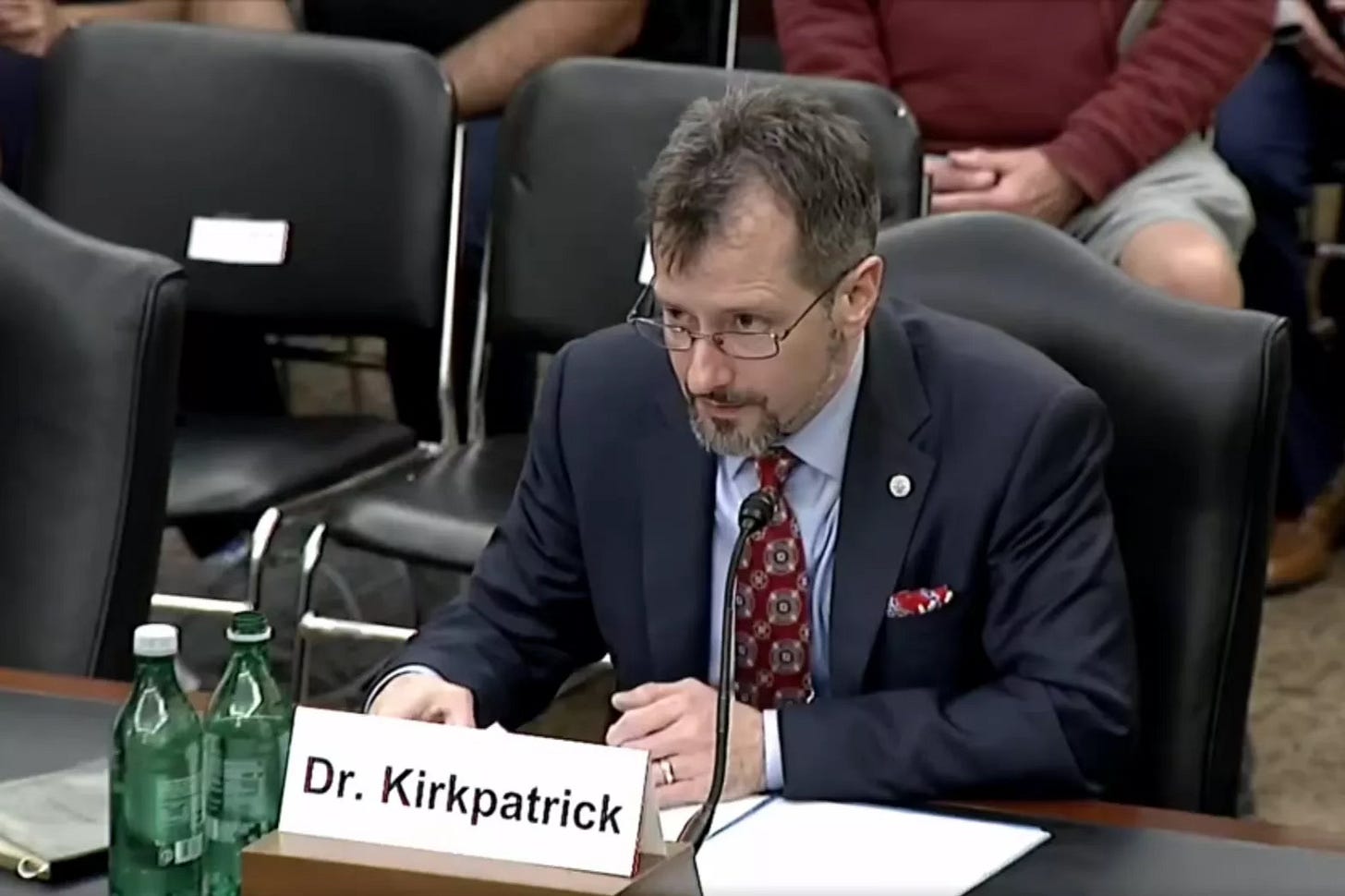 Sean Kirkpatrick speaking into a microphone at a congressional hearing, with a nameplate reading Dr. Kirkpatrick.
