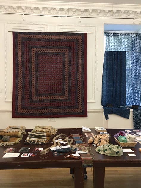 Views of the main exhibition space for Threads of Change at the Nehru Centre showing garments and fabric hanging on the walls with textile artefacts and books on the wooden table.