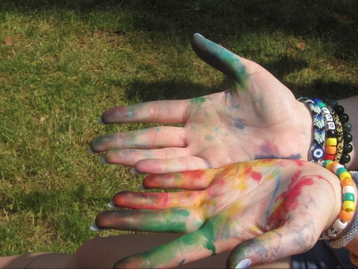 This may contain: a person with their hands painted in different colors on the grass and holding onto each other's hand This may contain: a person with their hands painted in different colors on the grass and holding onto each other's hand