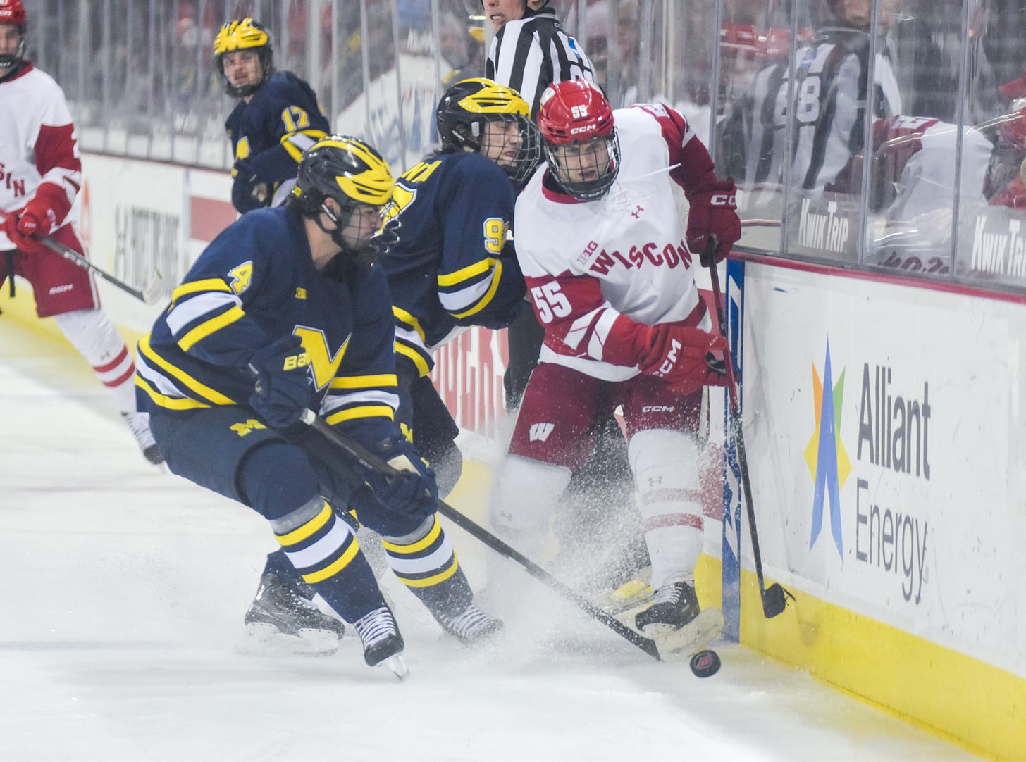 a pair of Michigan Wolverines skaters corner Wisconsin Badgers forward Oliver Tulk along the boards near the blue line a pair of Michigan Wolverines skaters corner Wisconsin Badgers forward Oliver Tulk along the boards near the blue line