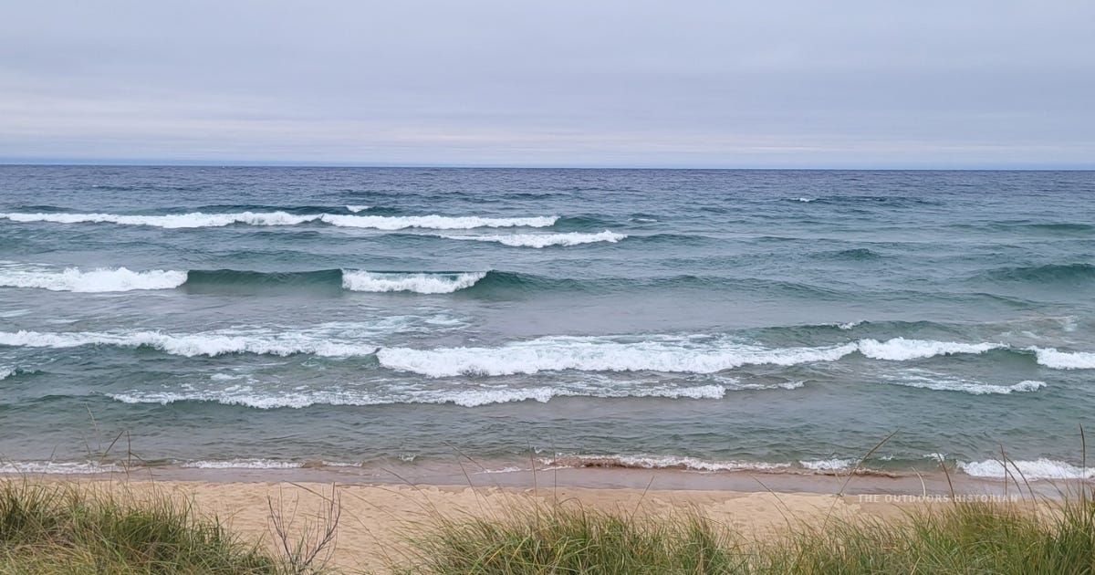 Rows of whitecapped waves rolling onto a sandy Lake Superior beach near Au Train, Michigan, under an overcast sky, with dune grass in the foreground. Rows of whitecapped waves rolling onto a sandy Lake Superior beach near Au Train, Michigan, under an overcast sky, with dune grass in the foreground.