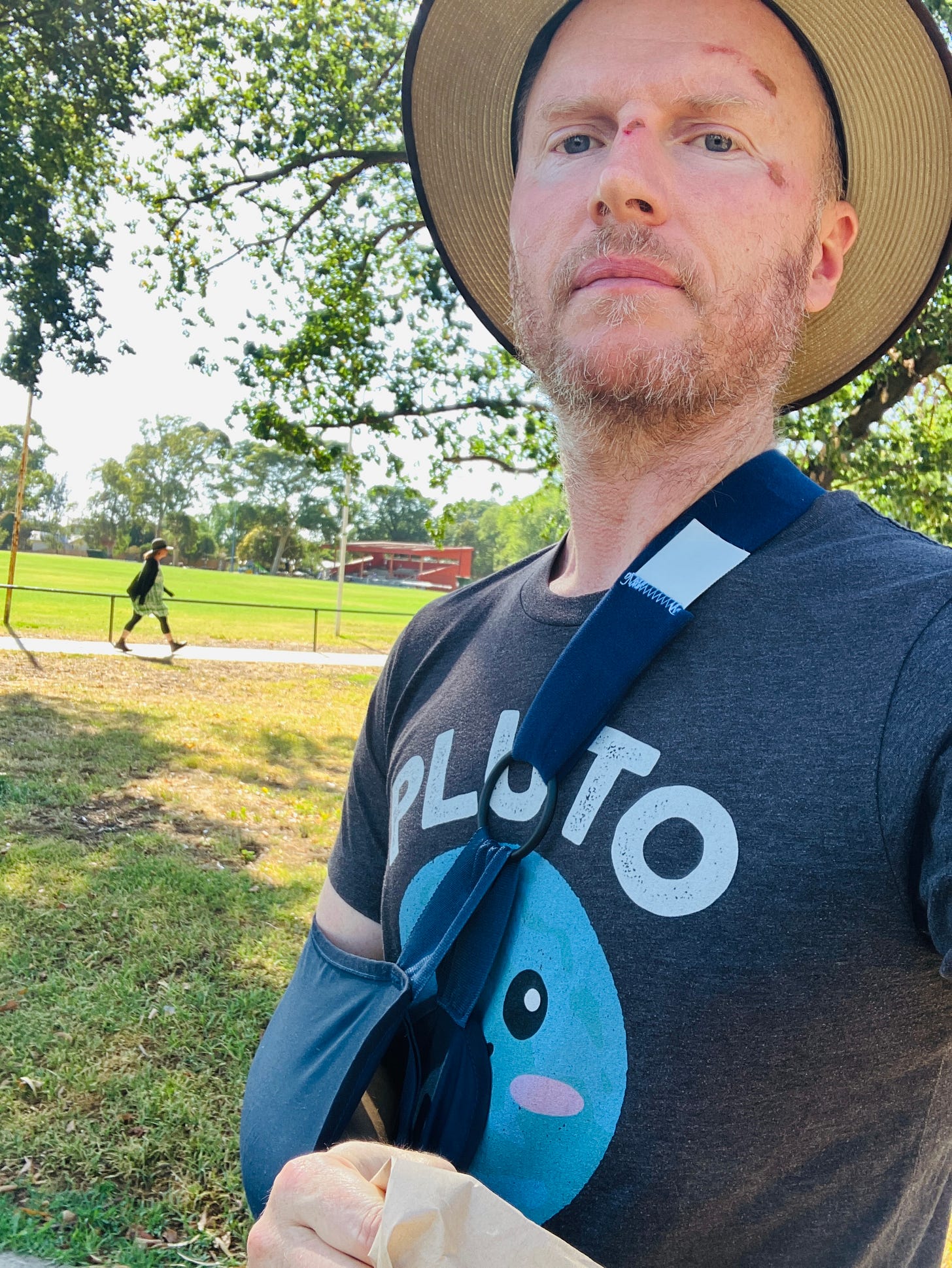 Photo of me in Fleming Park, wearing a hat and with my arm in a sling post-bike crash