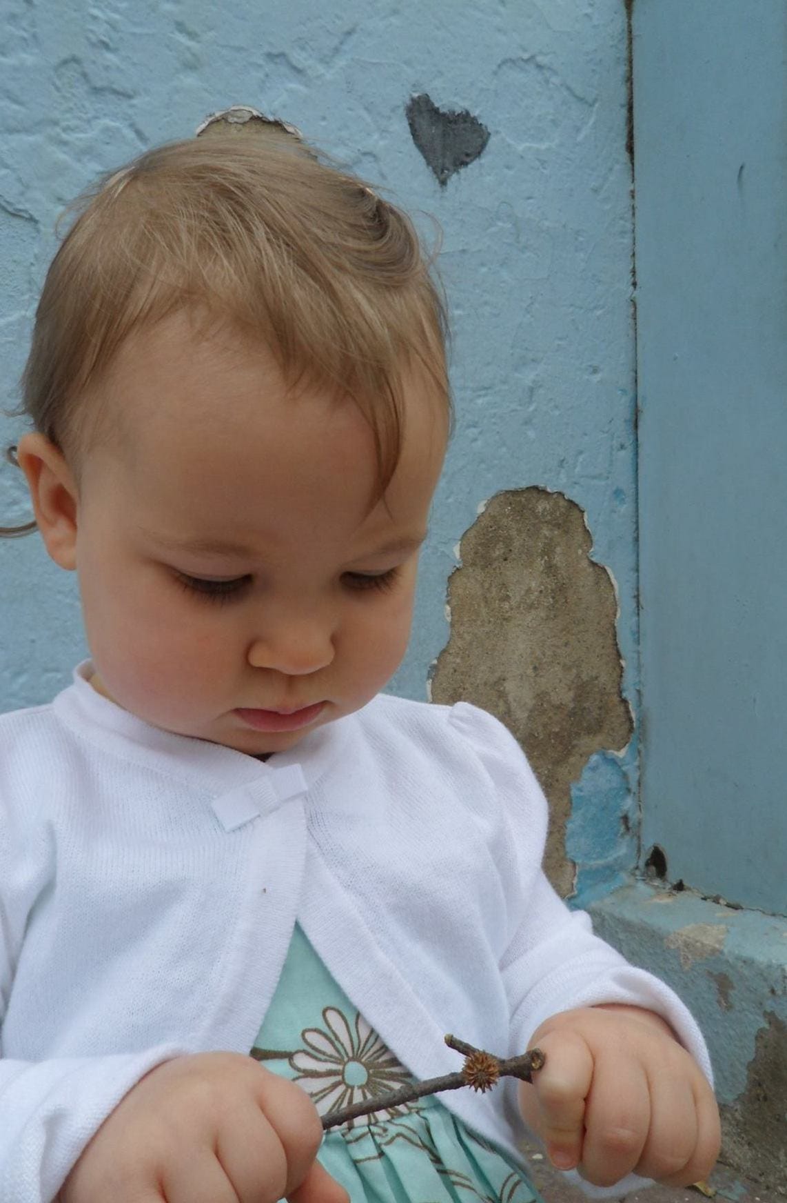A baby plays with sticks in front of a heart doodle on a wall