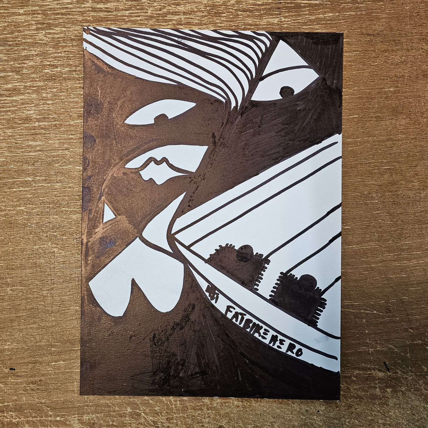 Alt Text: An abstract black and bronze ink drawing on white paper featuring a stylized, sharp-eyed face with flowing striped hair on the left, juxtaposed against a geometric, boat-like structure on the right containing two dark figures. The text "FATBIKEHERO" is written along the curved hull of the structure.