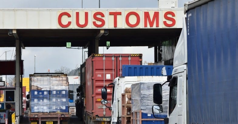 A line of trucks at a customs border post, with industrial goods, under overcast skies. A line of trucks at a customs border post, with industrial goods, under overcast skies.