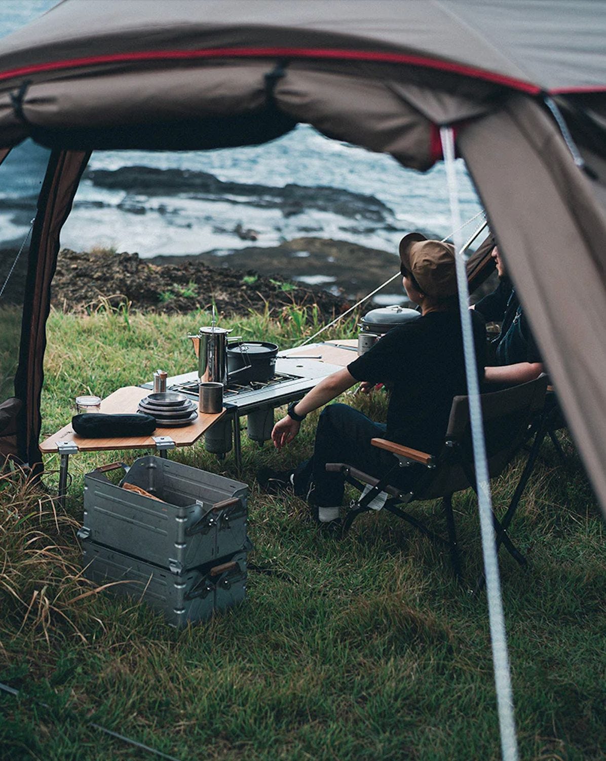 Person sitting outside a tent overlooking the sea Person sitting outside a tent overlooking the sea