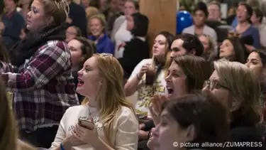 A crowd of young people at an election night party in November 2018. Several young women in the foreground are cheering. A crowd of young people at an election night party in November 2018. Several young women in the foreground are cheering.