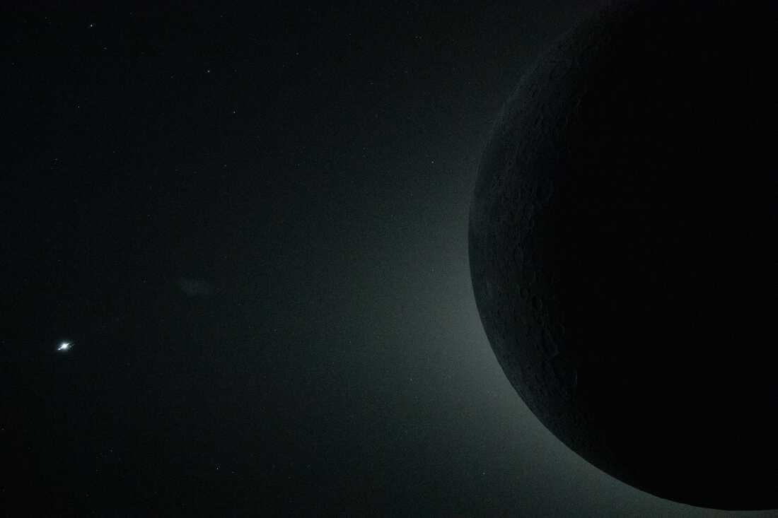 art002e009298 (April 6, 2026) – A close-up view from the Orion spacecraft during the Artemis II crew’s lunar flyby on April 6, 2026, captures a total solar eclipse, with only part of the Moon visible in the frame as it fully obscures the Sun. Although the full lunar disk extends beyond the image, the Sun’s faint corona remains visible as a soft halo of light around the Moon’s edge. From this deep-space vantage point, the Moon appeared large enough to sustain nearly 54 minutes of totality, far longer than total solar eclipses typically seen from Earth. This cropped perspective emphasizes the scale of the alignment and reveals subtle structure in the corona during the rare, extended eclipse observed by the crew. The bright silver glint on the left edge of the image is the planet Venus. The round, dark gray feature visible along the Moon’s horizon between the 9 and 10 o’clock positions is Mare Crisium, a feature visible from Earth. We see faint lunar features because light reflected off of Earth provides a source of illumination.