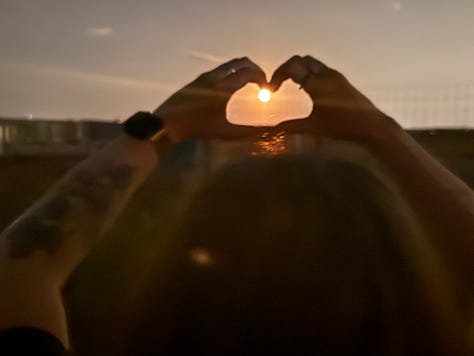 photo 1: meg's hands make a heart shape to frame the moon, which looks like a sun. photo 2: Andrea wears a shirt with a moon on it and holds up a sign that says "I'd rather have a sky without a moon in it than a poem without a moon it in." Photo 3: an excited, bewildered Megan tries to point to the giant moon in the sky. her aim is off.