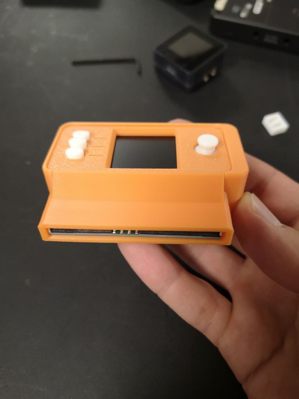 The assembled orange 3D-printed SeedSigner enclosure held in one hand, with the smartcard slot visible along the bottom edge. The assembled orange 3D-printed SeedSigner enclosure held in one hand, with the smartcard slot visible along the bottom edge.
