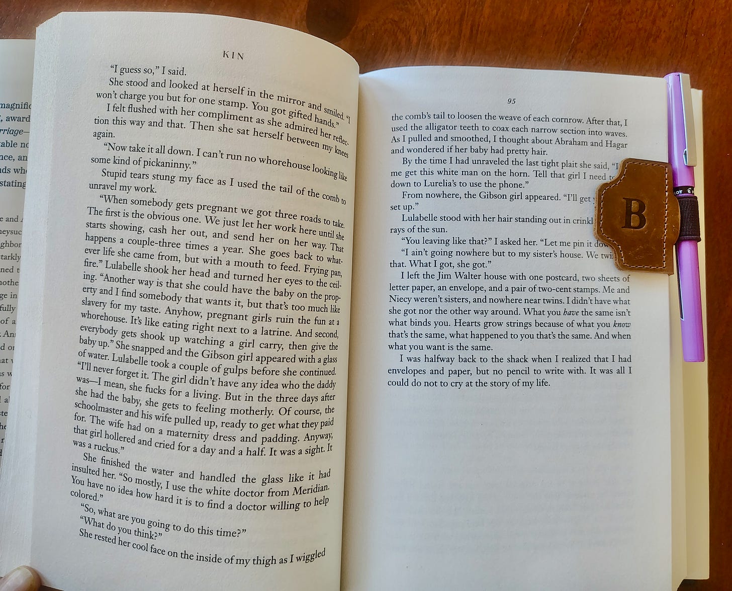 book titled Kin by tayari jones held open by a leather bookmark that is small and clips to the side of the page. the bookmark has an elastic loop that holds a lavender pen