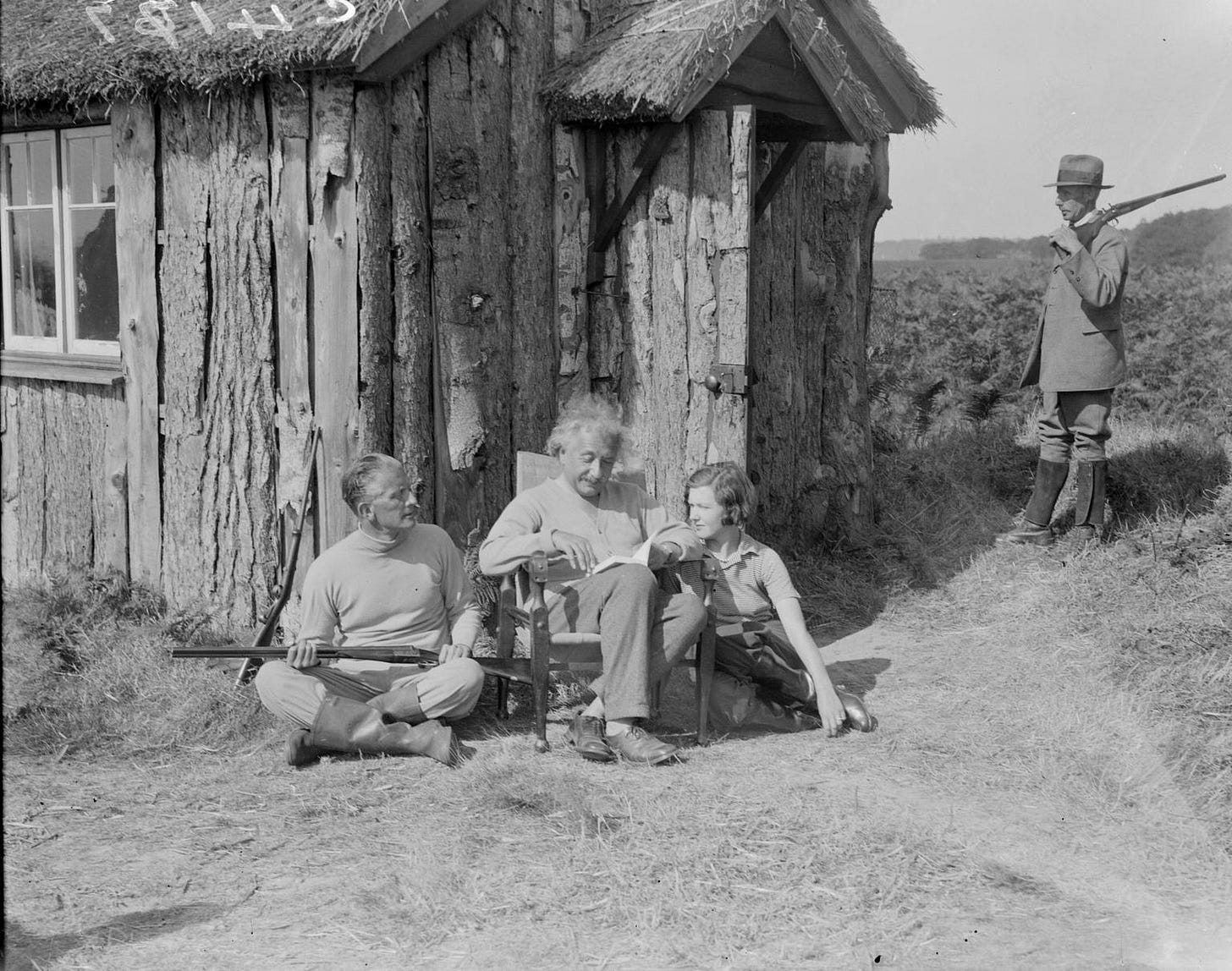 Einstein sitting outside a small wooden cottage near Cromer in Norfolk, England. He was the guest of Commander Oliver Locker-Lampson, who sits on the ground next to the professor carrying a shotgun. Oliver had offered refuge to Einstein to help him avoid persecution by the Nazis. 1933.
