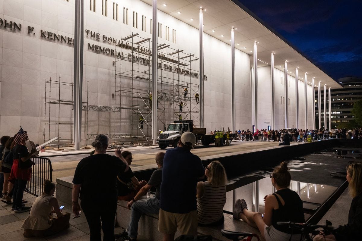 Spectators watch as workers put up scaffolding ahead of a court-mandated deadline to remove President Donald Trump’s name from the Kennedy Center by Saturday.  (Craig Hudson/For the Washington Post)