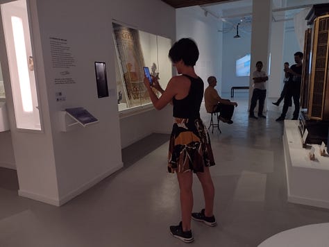 1- Fotografía de una cartelería externa de un museo, hecha de estructura de metal de aproximadamente unos tres metros de altura y sesenta centimetros de ancho. Se encuentra ubicado en el medio de un parque, en un sector donde hay tránsito peatonal. En la cartelería hay pictogramas que indican los espacios, servicios, contenidos y actividades de el museo castagnino 2- Fotografía de una cartel externa de un museo ubicado en el jardin previo al ingreso al edificio. El cartel es un rectángulo horizontal con un pie metalico que entra en el suelo. Da la bienvenida y expone pictogramas que indican los espacios, servicios, contenidos y actividades con los que cuenta el museo. 3- Fotografia de una pared en el interior de un museo. la pared esta pintada de negro y tiene en color blanco la leyenda con el nombre dle museo nacional del grabado y un texto. Al costado derecho hay un listado de pictogramas que indican los espacios, servicios, contenidos y actividades con los que cuenta el museo. 4- Fotografia de una pared en el interior de un museo. la pared es blanca y tiene en el centro un recuadro con borde negro y en su interior un texto que da la bienvenida. Debajo hay un listado de pictogramas que indican los espacios, servicios, contenidos y actividades con los que cuenta el museo. 5- Fotografia de un sector de una exhibición. En la pared hay cuatro imagenes enmarcadas y debajo en un exhibidor hay folios aillados con documentos antiguos y otras imagenes. En un costado se encuentra un pictograma y un código qr. 6-Fotografia de una sala de exhibición de un museo de arte contemporaneo. En el centro hay una mujer de pie agarrando el celular con las dos manos para sacar una fotografia a un dispositivo que hay en una de las paredes de la exhibición. detrás de ella, al final de la sala hay mas personas de pie y sentadas.