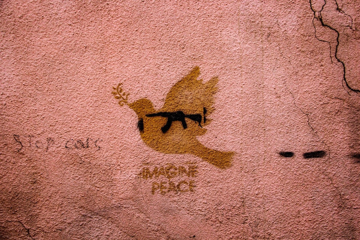 A dove painted on a wall with a gun painted over the dove. The words "imagine peace" are written below the dove and gun. A dove painted on a wall with a gun painted over the dove. The words "imagine peace" are written below the dove and gun.