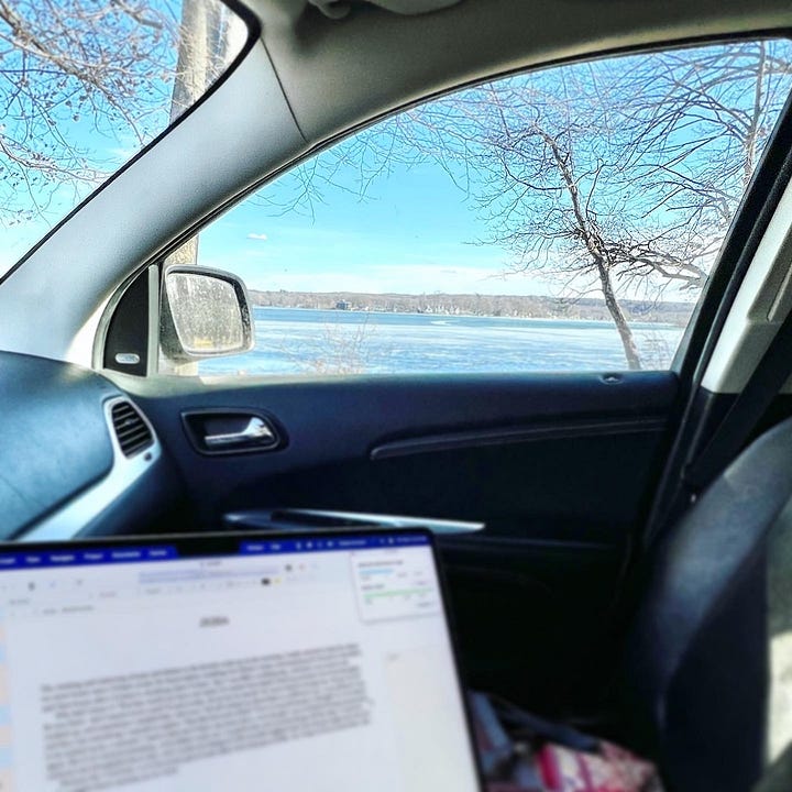 author sitting in car with laptop writing book with a view of the lake in the background